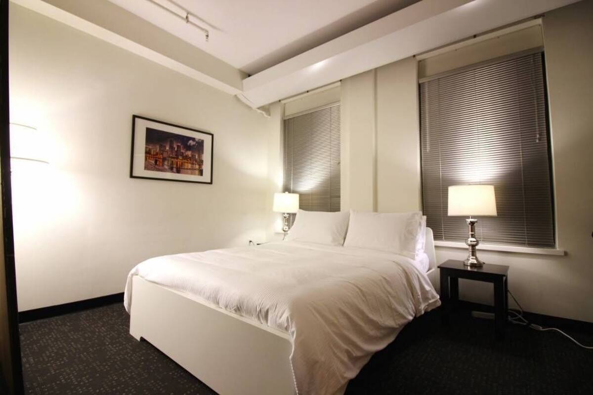 Habitación de hotel con una cama, dos lámparas de noche, una ventana con persianas y un cuadro en la pared.