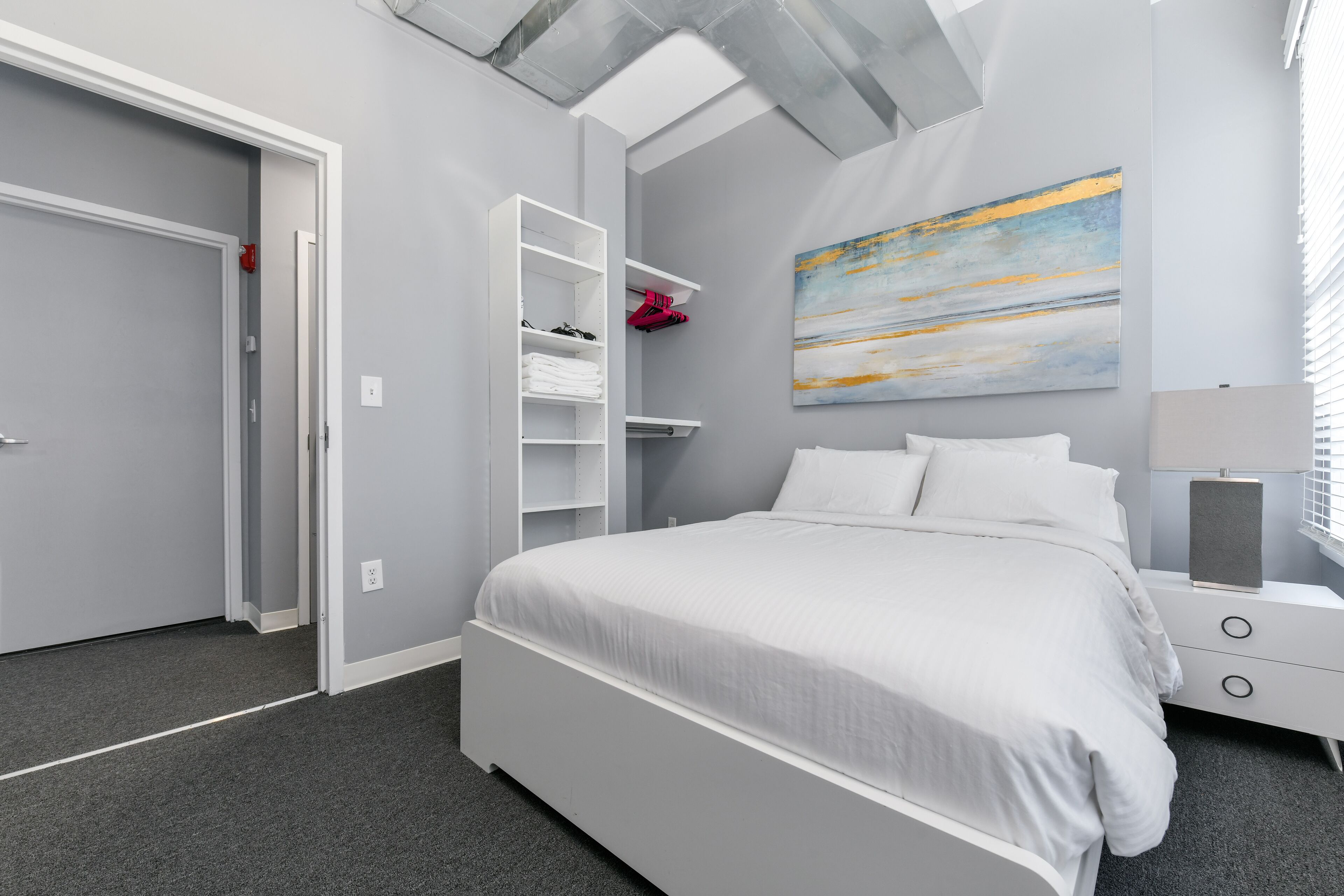 A modern bedroom with a bed, a wardrobe, a nightstand, and a painting on the wall.
