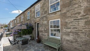 A stone building with a patio area featuring a table, chairs, and a bench. - Homely Cottage with Sun Terrace, Short Walk to Beach (Porthleven)