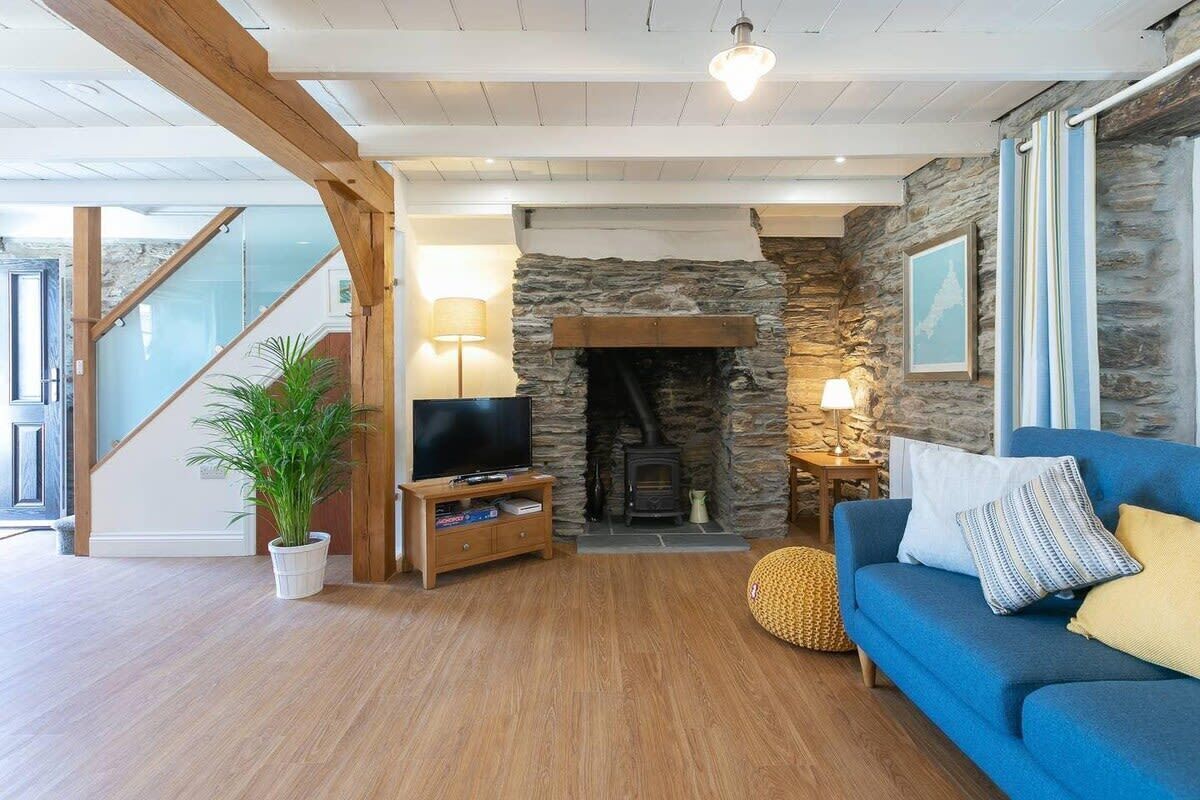 A living room with a stone fireplace, a television on a wooden stand, a blue sofa, and a staircase.