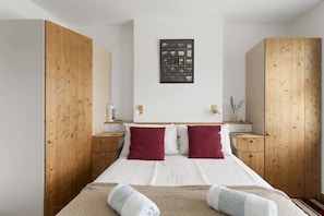 A bedroom with a bed, wooden wardrobe, bedside tables, a wall-mounted picture, and a red rug.
