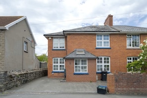 A two-story brick house with a tiled roof, a small front porch, and a stone wall on the left.