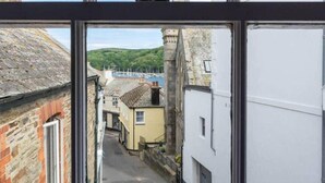 A narrow street with buildings on either side, a clear sky, and a distant view of a harbor with boats. - Sundance Cottage, Central Fowey with Sea Views! (Cornwall)