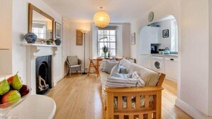 A cozy living room with a fireplace, a sofa, a dining area, and a kitchen. - Sundance Cottage, Central Fowey with Sea Views! (Cornwall)