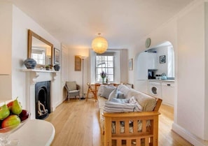 A cozy living room with a fireplace, a sofa, a dining area, and a kitchen. - Sundance Cottage, Central Fowey with Sea Views! (Cornwall)