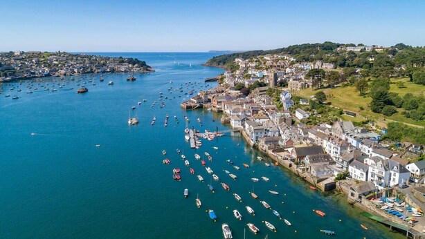 Une ville côtière dotée d’un port rempli de bateaux, de bâtiments historiques et surplombée d’un ciel bleu azur.