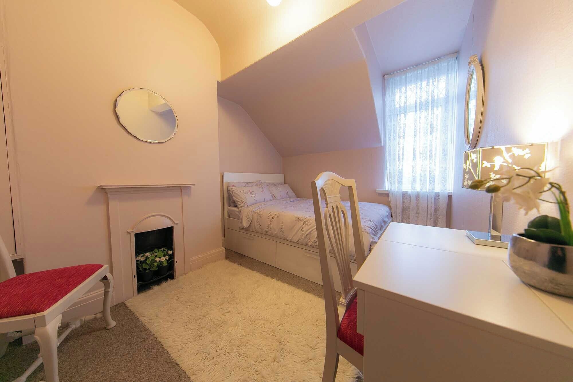 A bedroom with a bed, a desk, a chair, a fireplace, and a mirror on the wall.
