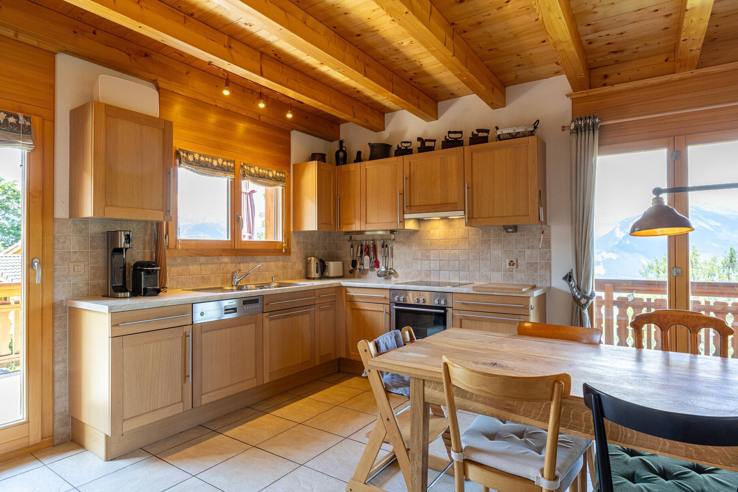 A kitchen with wooden cabinets, a dining table, and chairs. There is a window with a view of mountains.