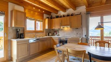 A kitchen with wooden cabinets, a dining table, and chairs. There is a window with a view of mountains.
