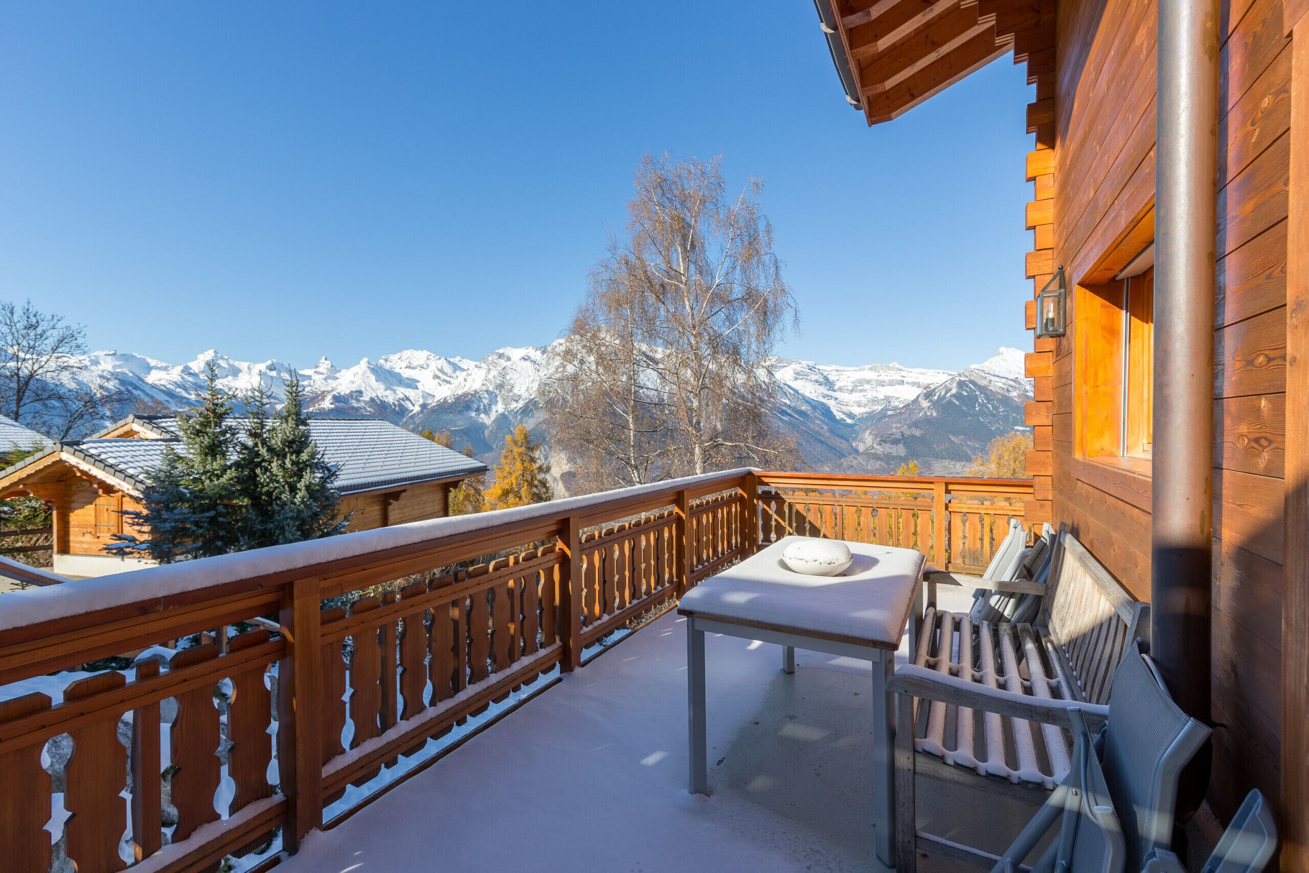 Ein Holzbalkon mit Tisch und Stühlen, mit Blick auf schneebedeckte Berge.