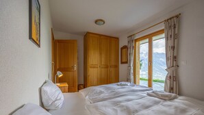 A bedroom with two beds, wooden wardrobe, and a window with a mountain view. - Chalet Le Papillon, sauna, 4 Vallées (Haute-Nendaz)