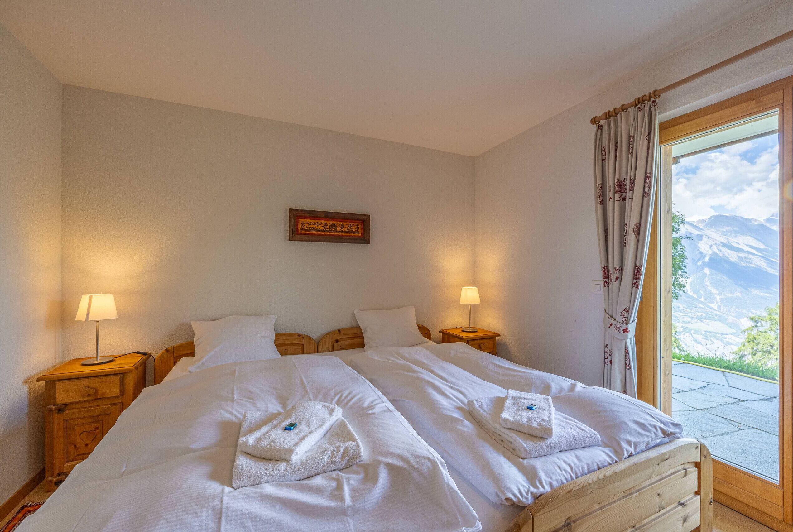 A bedroom with two beds, wooden headboards, bedside lamps, a framed picture on the wall, and a window with curtains.