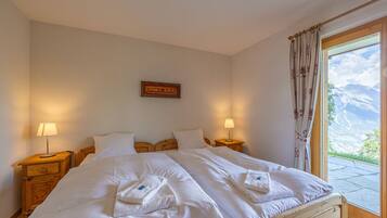 A bedroom with two beds, wooden headboards, bedside lamps, a framed picture on the wall, and a window with curtains.