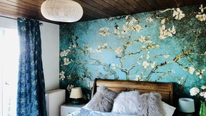 Una camera da letto con un letto di legno, una parete decorata con motivi floreali blu, un termosifone bianco e una lampada a sospensione.