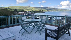 Una terrazza con tavolo e sedie che si affaccia su un lago, con vista su una città e delle colline.