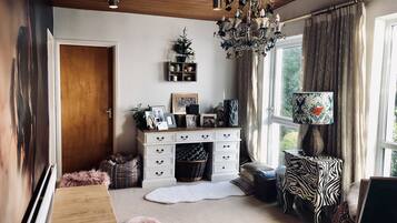 A cozy living room with a wooden ceiling, a chandelier, a white cabinet with drawers, a window with curtains, and a zebra-patterned chair.
