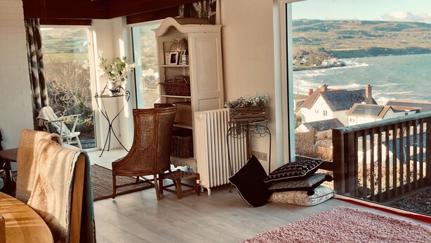 Un accogliente soggiorno con vista sul mare, pavimento in legno, un'ampia finestra e una libreria.