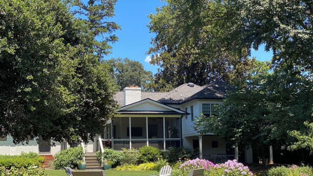 Una casa a due piani con un portico coperto, immersa nel verde e circondata da un giardino curato.