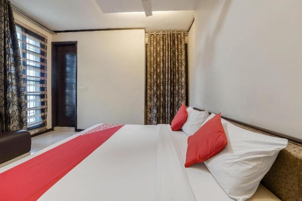 Una habitación de hotel con una cama, un ventanal con cortinas, una puerta y una pared con interruptor de luz.