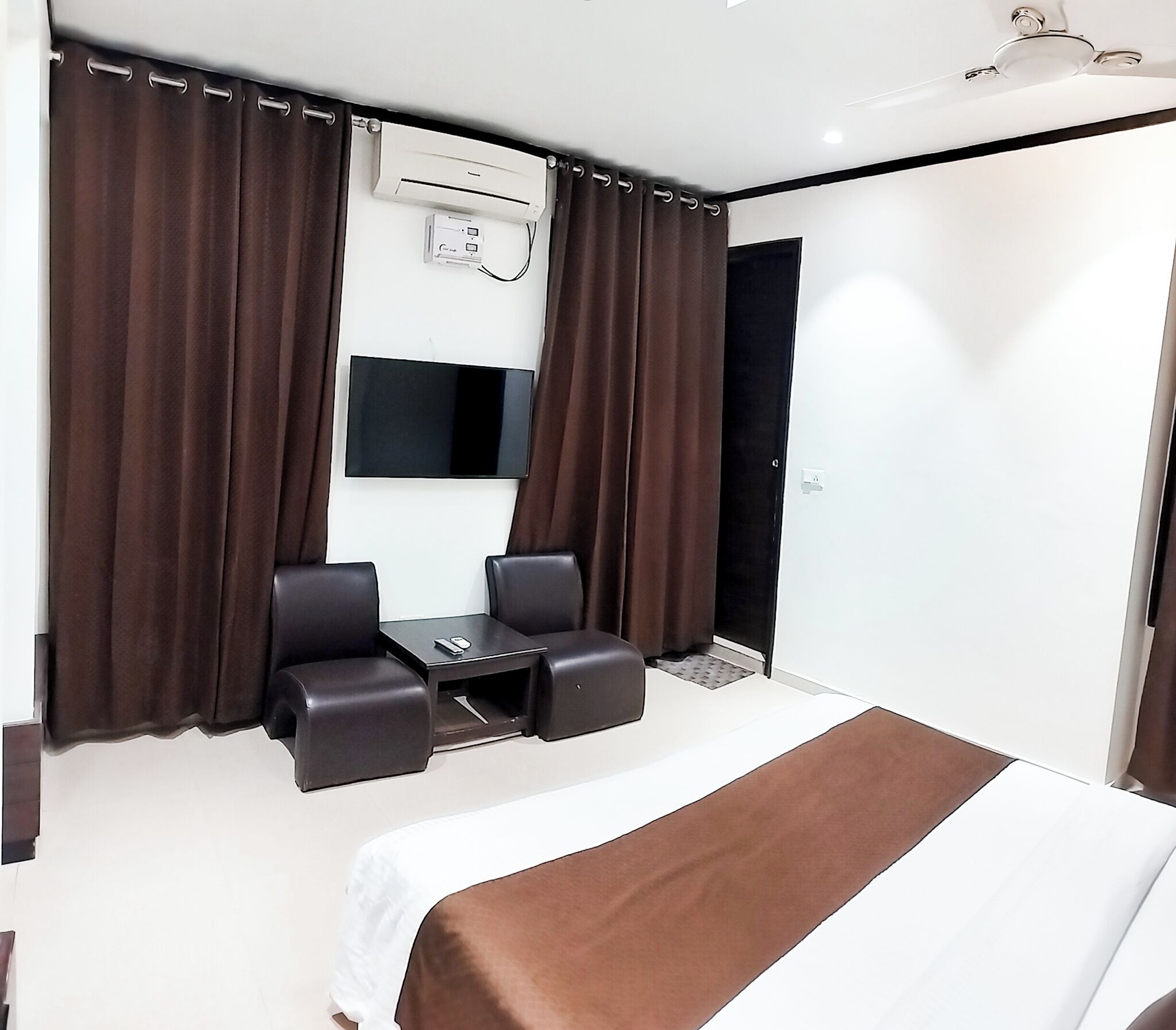 A hotel room with a bed, a desk, two chairs, a flat-screen TV, and a window with curtains.