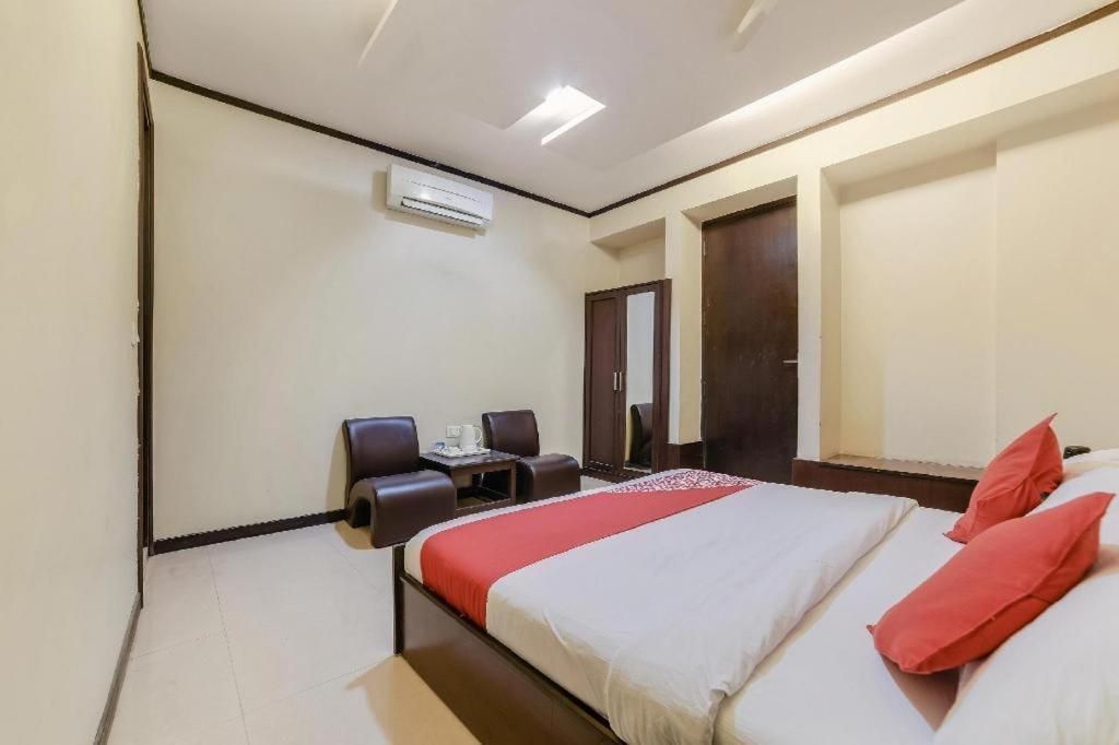 A hotel room with a bed, a desk, two chairs, and an air conditioning unit.