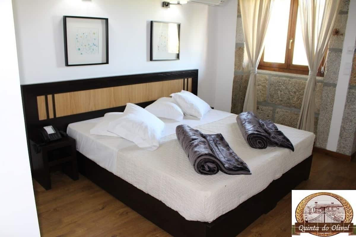 A neatly made bed with white linens and rolled towels, a bedside phone, and framed artwork on the wall.