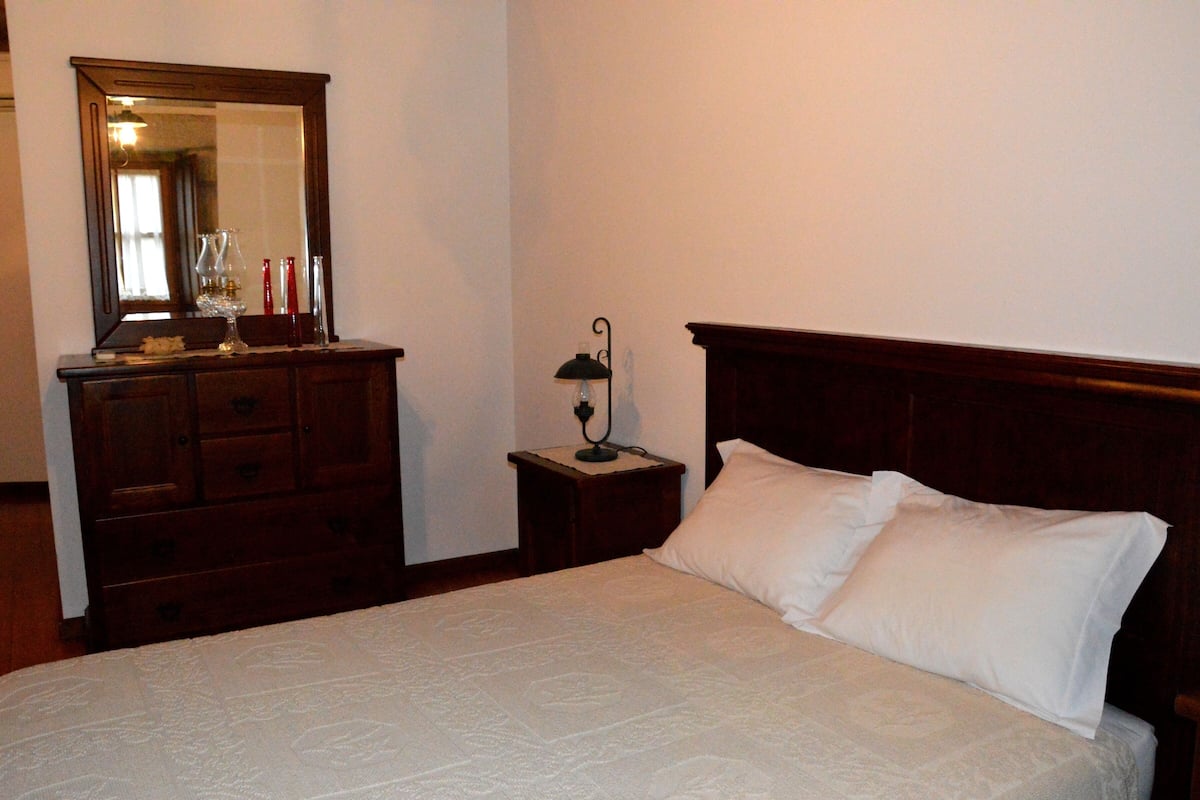 A bedroom with a wooden bed, a nightstand with a lamp, a dresser, and a mirror.