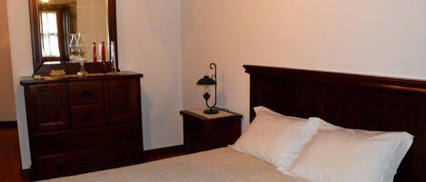 Un dormitorio con una cama de madera, una mesita de noche con lámpara, un tocador y un espejo.