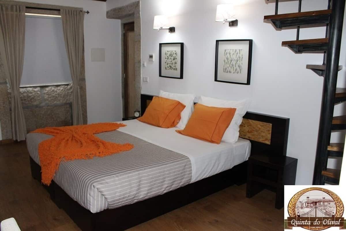 A hotel room with a bed, two framed artworks on the wall, a wooden headboard, and a staircase.