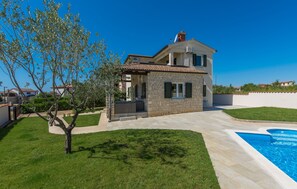 Ein zweigeschossiges Haus mit einer Stein-Fassade, einem Schwimmbad und einem gepflegten Rasen.