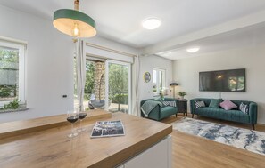 Ein modernes Wohnzimmer mit einem Couchtisch aus Holz, zwei Weingläsern, einem grünen Sofa und einem großen Fernseher an der Wand.