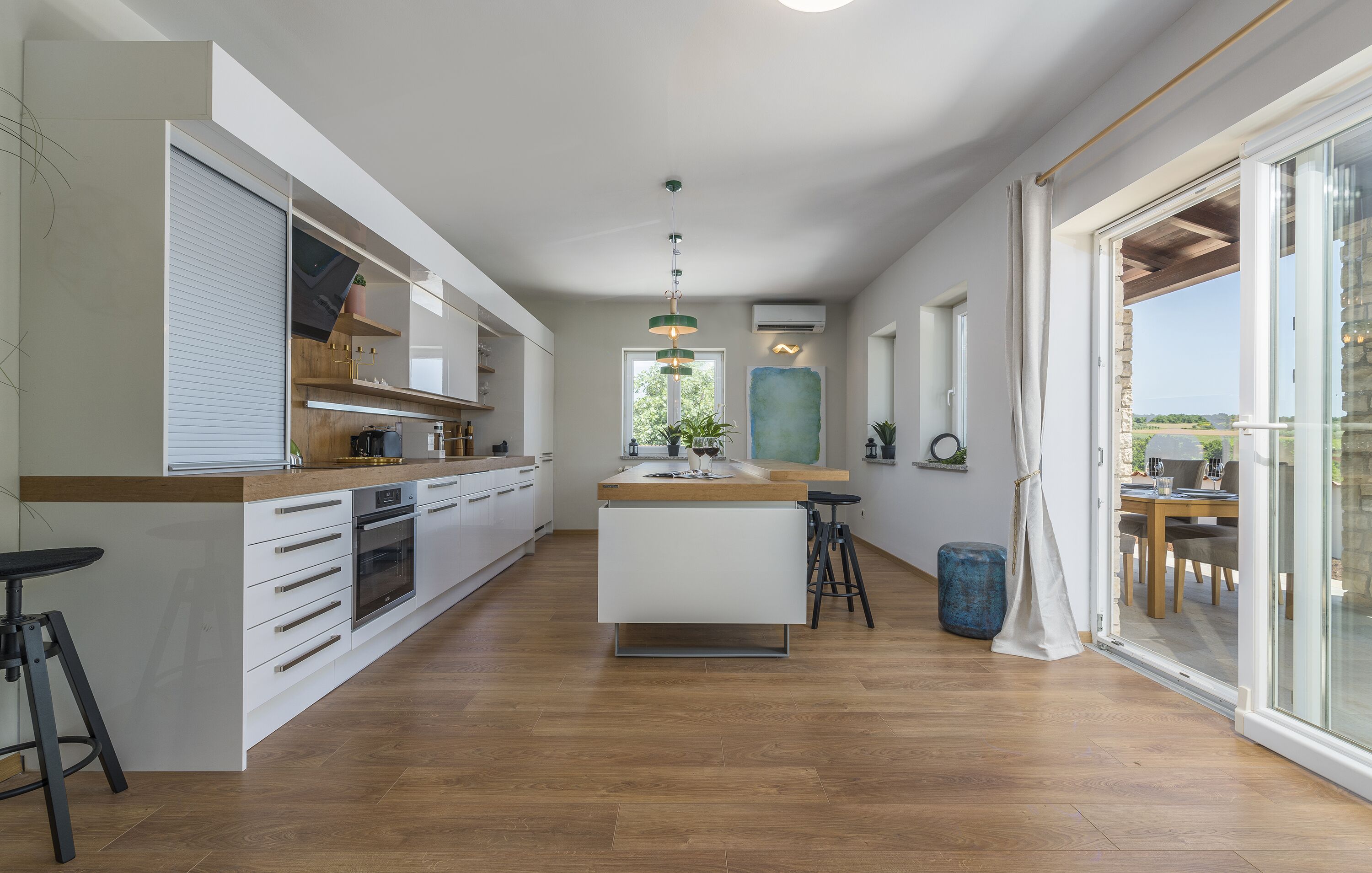 A modern kitchen with a central island, wooden flooring, and a large sliding glass door leading to an outdoor area.