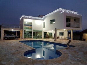 A modern two-story house with a swimming pool, stone patio, and a car parked in the driveway.