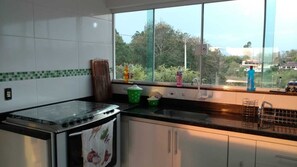 A kitchen with a stove, sink, and window overlooking greenery.