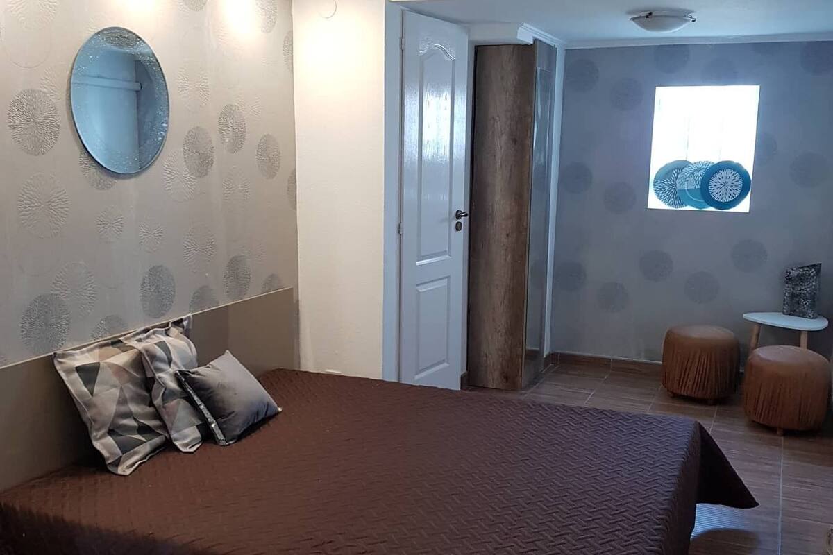 A bedroom with a large bed, a round mirror, a door, and a window with a view.
