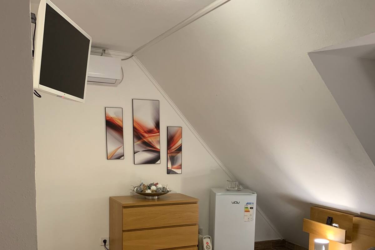 A modern bedroom with a bed, a dresser, a refrigerator, and abstract wall art.
