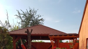 A patio with a wooden pergola, a hammock, a fire pit, and a small table. - Airport16 B&B (Vecsés)