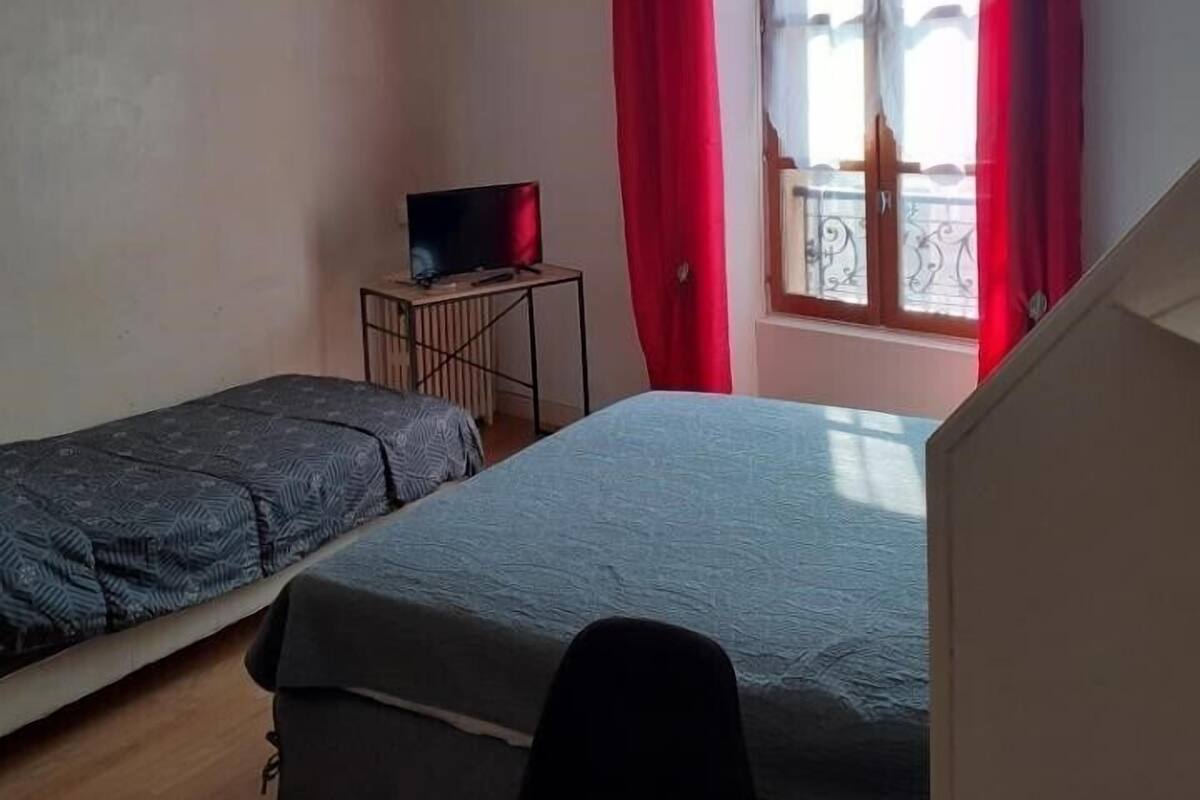 A small, simple room with two single beds, a small table with a TV, and a window with red curtains.