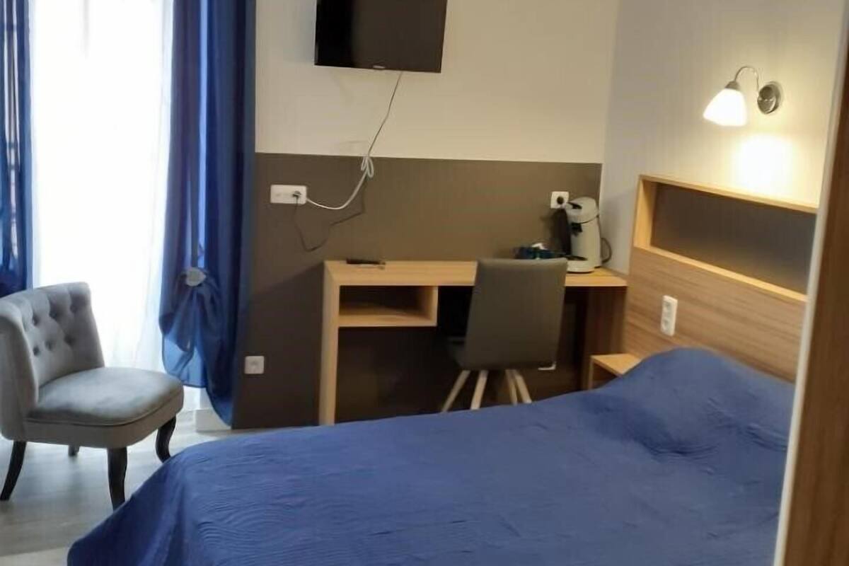 A hotel room with a bed, a desk, a chair, a television, and a lamp.