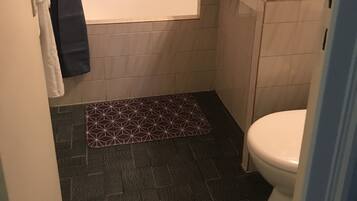 Un bagno piccolo con una vasca, un lavandino e un water. Sul pavimento c'è un tappeto scuro e un portasacchi con degli asciugamani.