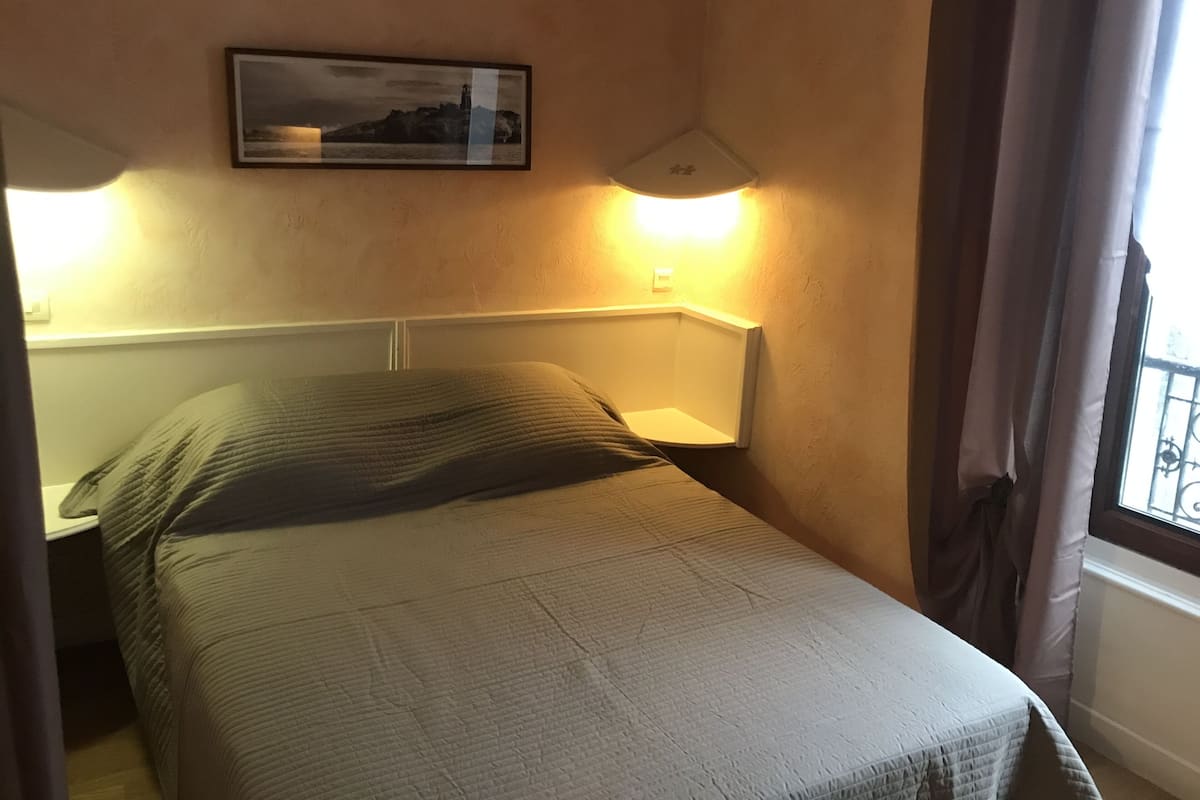 A hotel room with a bed, a nightstand, a wall-mounted lamp, and a framed picture.
