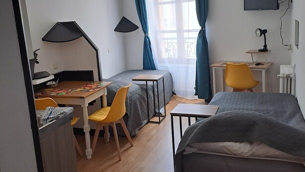 Habitación de hotel compacta con cama, escritorio con silla, una mesita, lámpara y televisor montado en la pared.