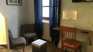 Una habitación pequeña y acogedora con un sofá, una silla de madera, una mesita y un televisor montado en la pared.
