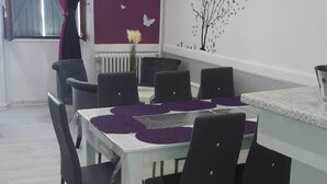 Un comedor con una mesa dispuesta para seis personas, rodeada de sillas, en una habitación con una pared de acento morada y un mural decorativo de un árbol.