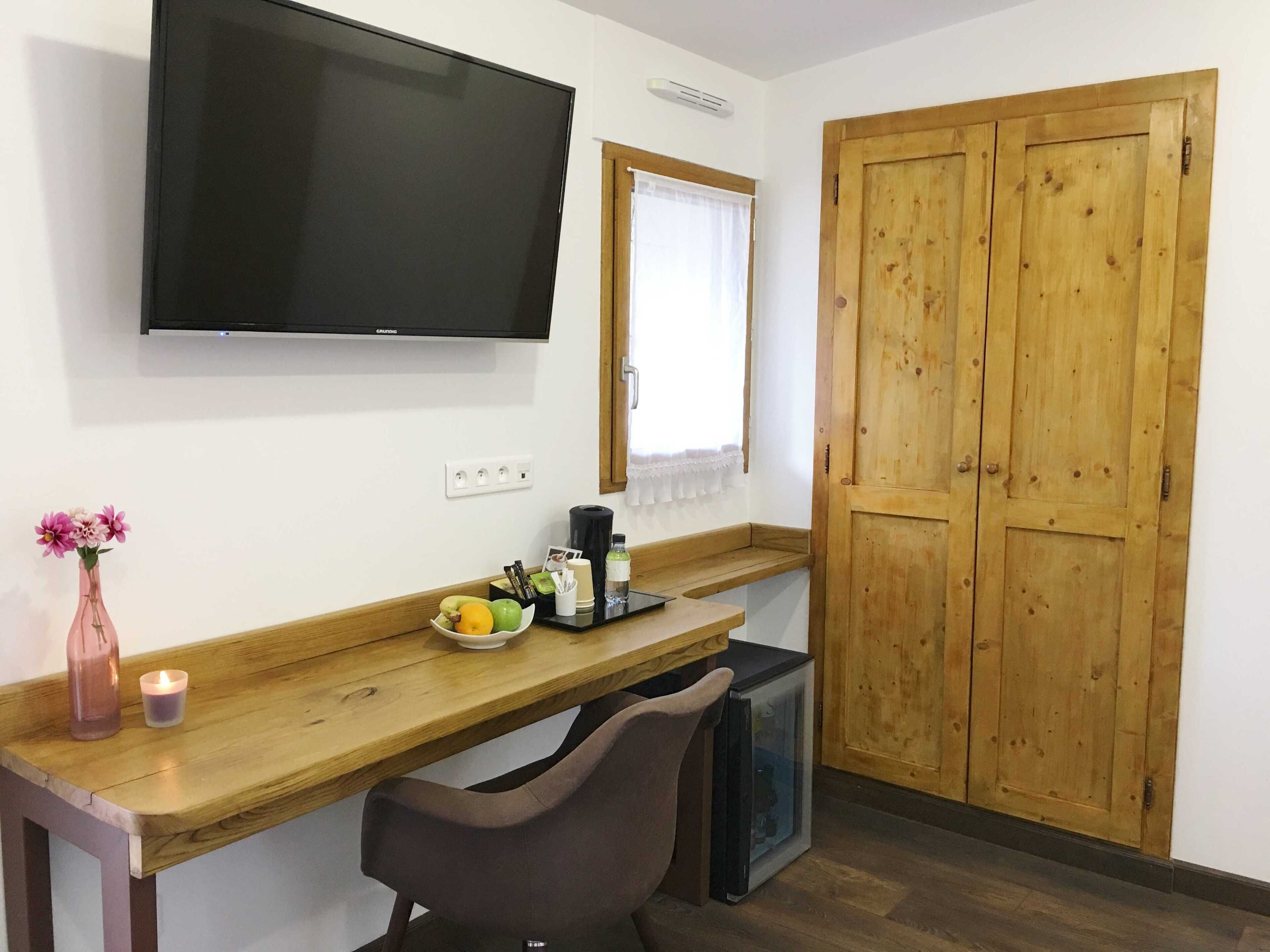 A small kitchenette with a wooden countertop, a TV mounted above it, and a wooden door to the right.