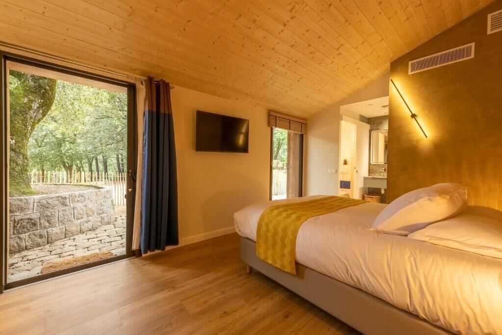 A bedroom with a bed, a television, a window with curtains, and a view of trees.