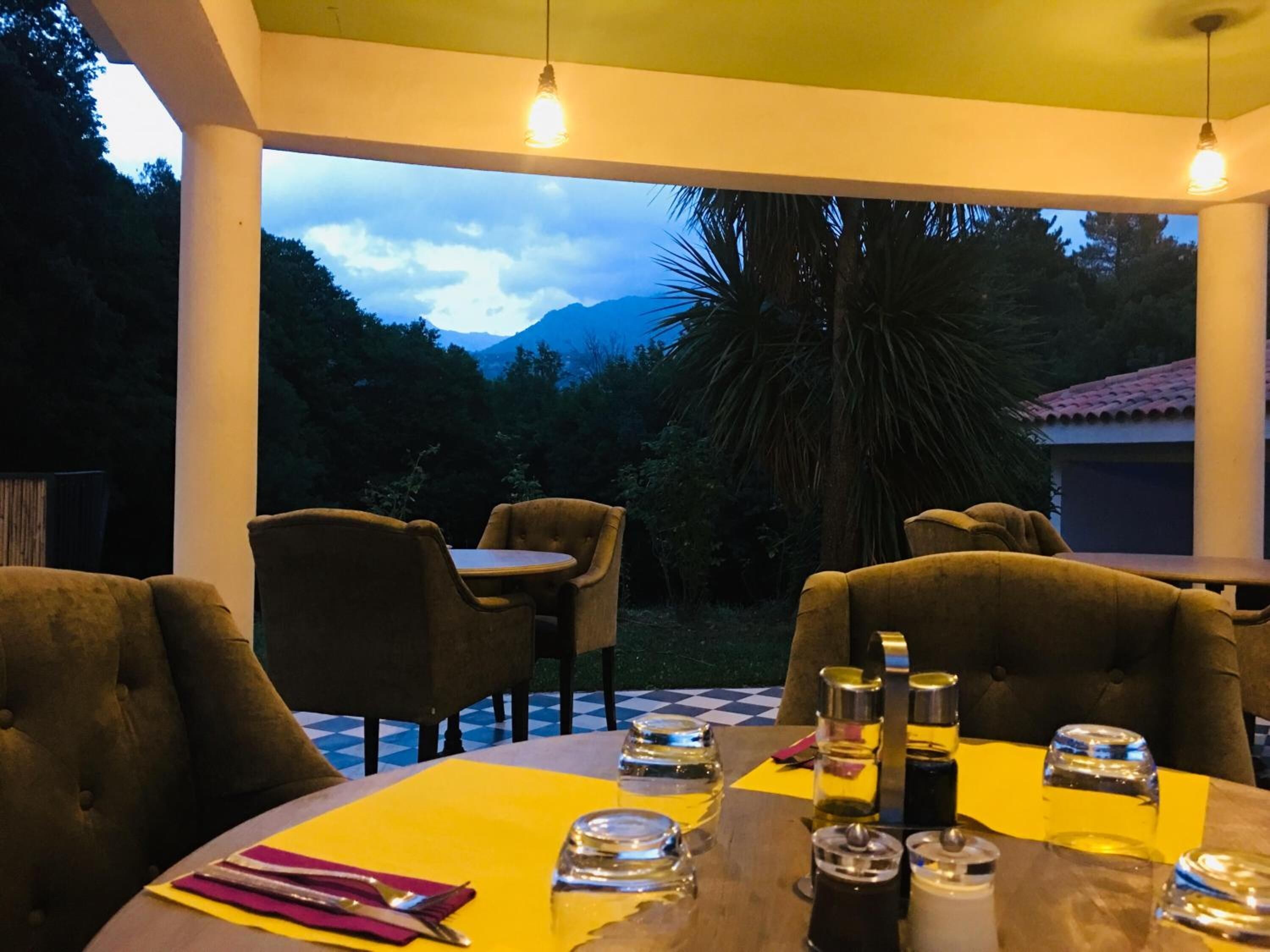 A dining area with a table set for two, surrounded by chairs, with a view of mountains and trees.