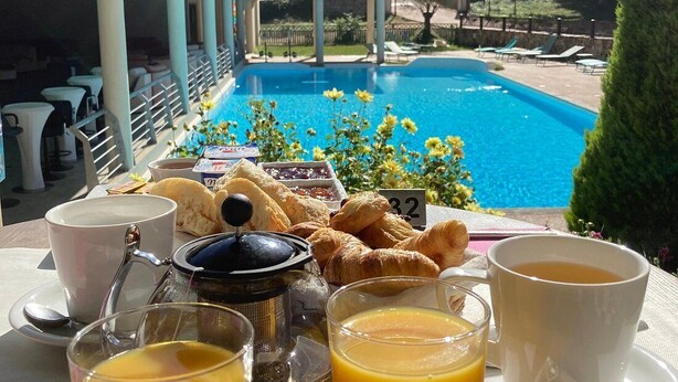 A breakfast setup with croissants, orange juice, and coffee on a table overlooking a swimming pool.