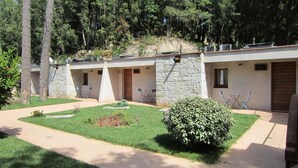 A row of stone buildings with outdoor seating areas, surrounded by greenery and trees.