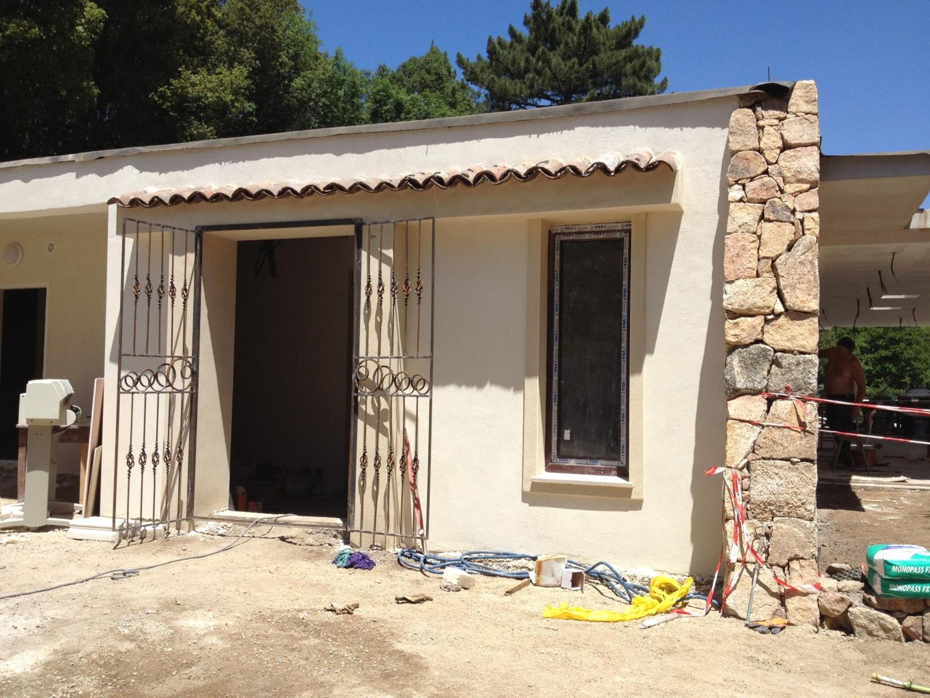 A building with a stone wall, a tiled roof, and a door with decorative metalwork.